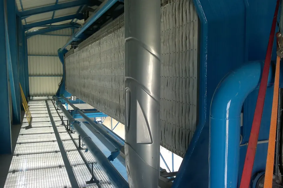 Große Kammerfilterpresse in einer Industriehalle: lange Reihe heller Filterplatten in einem blauen Stahlgestell, davor Rohrleitungen und ein Gitterrostboden