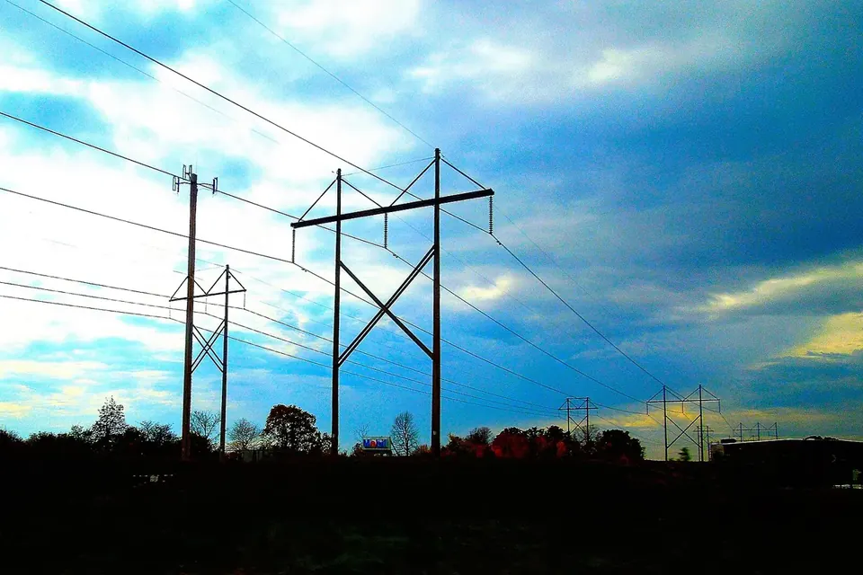 Silhouettes of high-voltage transmission towers and power lines against a blue evening sky