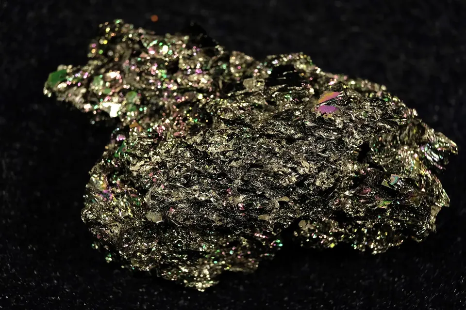 A large irregular lump of silicon carbide crystals with a metallic green and gold sheen on a black background