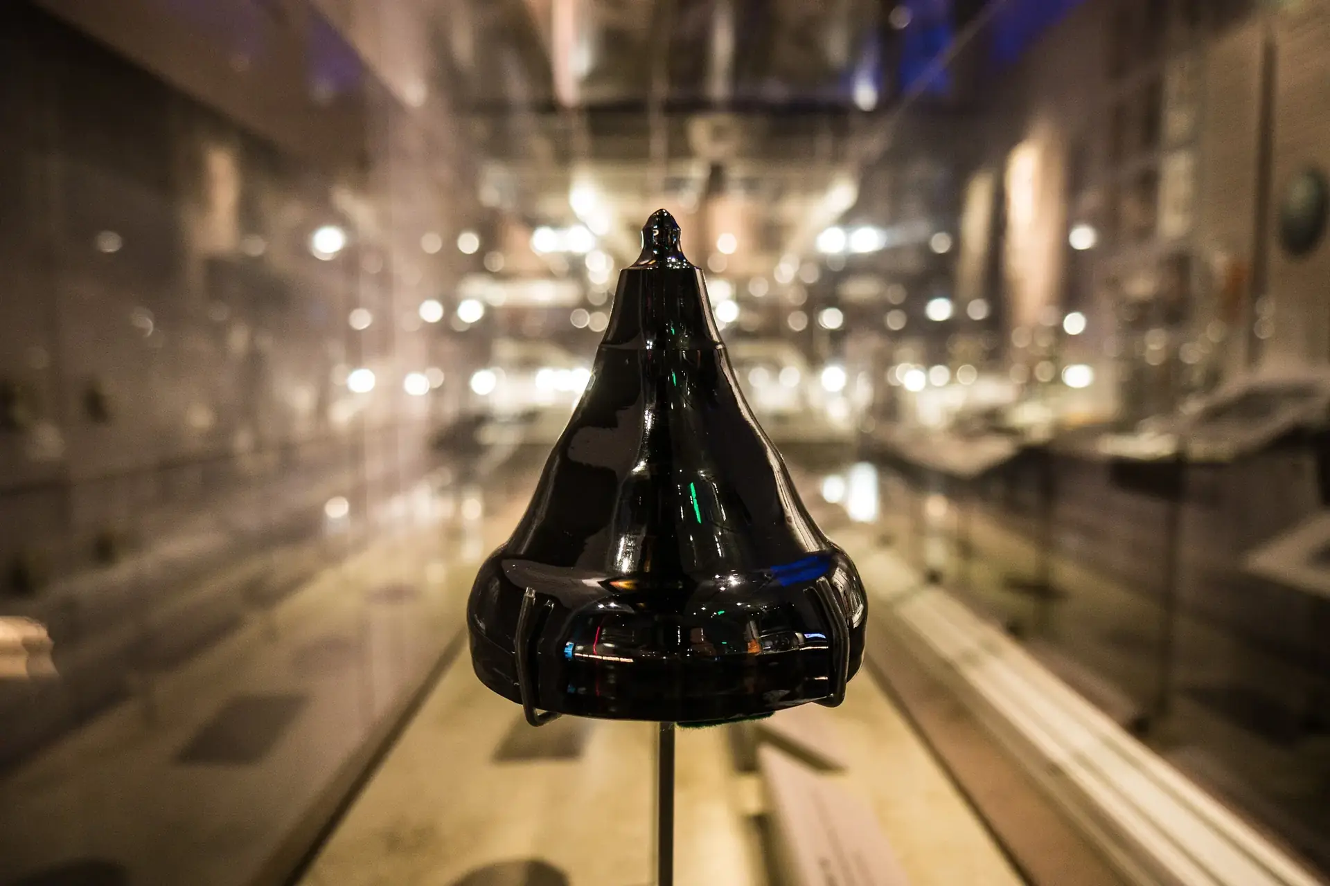 The conical tip of a glossy black silicon ingot in a lit museum display case